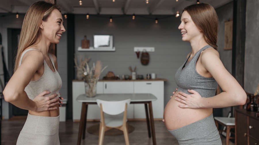 Due donne sorridenti in abbigliamento sportivo, una in gravidanza